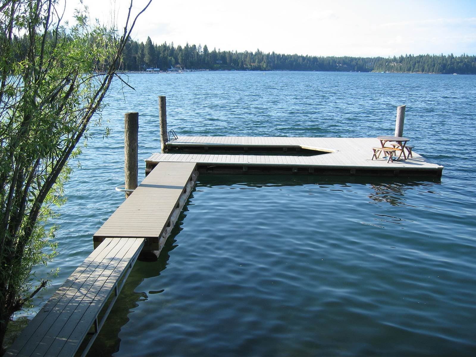 A floating dock on the clear blue water of Honeysuckle Bay, Hayden Lake, with forest on the far shore.