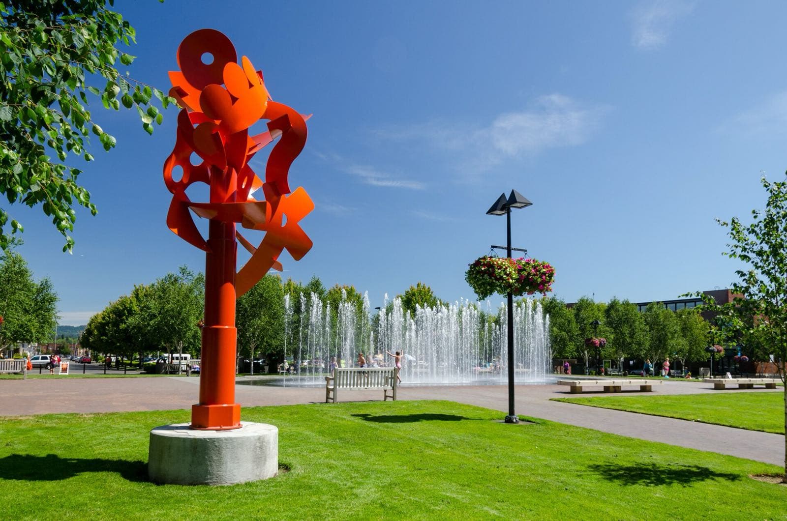 A bright red sculpture and splashing fountain in Beaverton City Park on a sunny day.