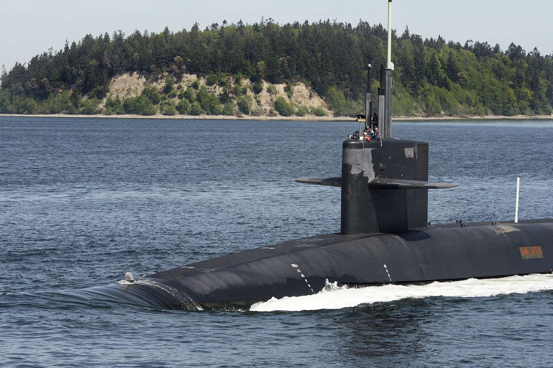 The ballistic-missile submarine USS Henry M. Jackson on the surface of Hood Canal, returning to Naval Base Kitsap-Bangor past a forested bluff.